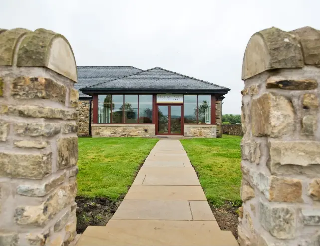 Stone-built clinic building with a path leading through a lawn to the entrance.